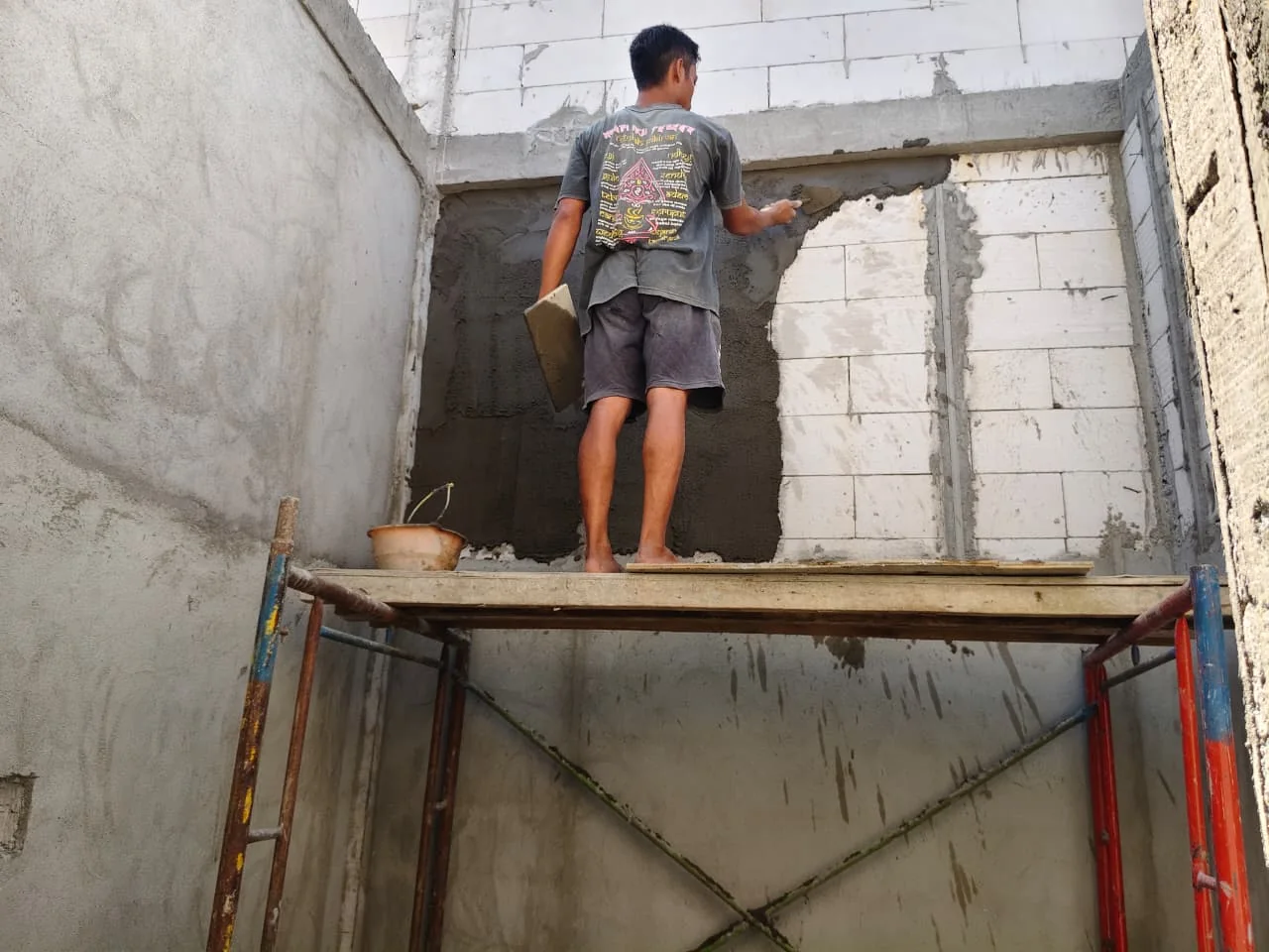 Tukang mengerjakan plesteran semen pada permukaan dinding bata ringan dalam renovasi bangunan